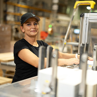 Kobieta w czapce pracuje przy maszynie w hali produkcyjnej.