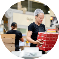 Kobieta w czepku pakuje czerwone pudełka na linii produkcyjnej w fabryce.